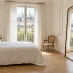 How to make a small bedroom look bigger: a bright white bedroom with a large floor mirror reflecting daylight from a window